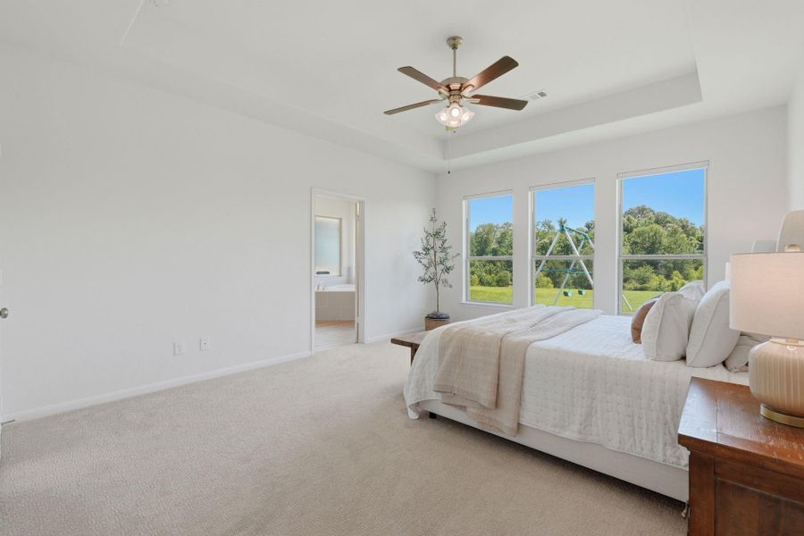 This spacious, bright primary bedroom features large windows with scenic views, a ceiling fan, and plush carpeting. It includes an en-suite bathroom and is tastefully decorated for comfort.