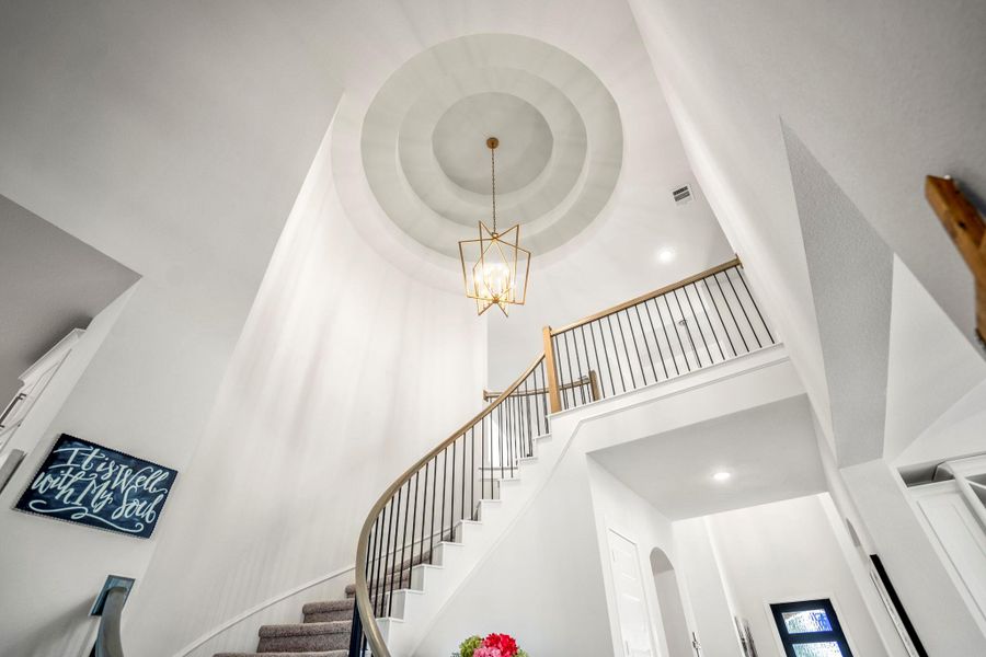 This photo showcases a grand, curved staircase with elegant railings, a striking chandelier, and high ceilings, creating a welcoming and luxurious entrance.