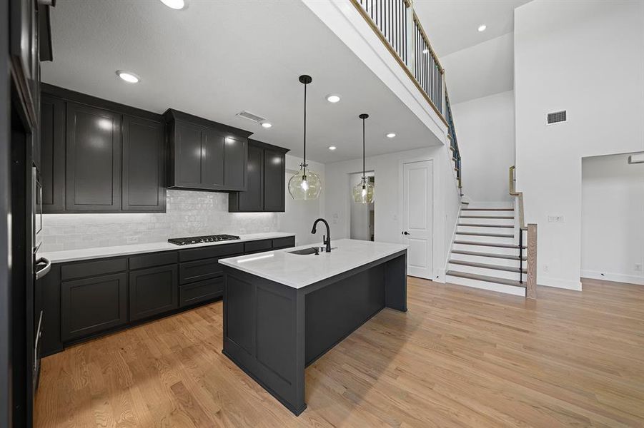 Kitchen with decorative backsplash, a kitchen island with sink, light stone countertops, decorative light fixtures, and light wood finished floors Kitchen with decorative backsplash, a kitchen island with sink, light stone countertops, decorative light fixtures, and light wood finished floors