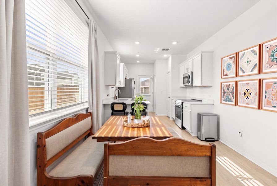 A well-lit kitchen with sleek appliances and light wood flooring offers comfortable banquette seating.
