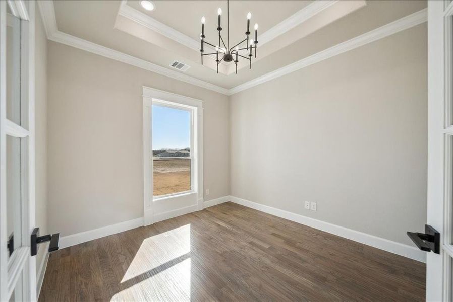 Unfurnished room featuring an inviting chandelier, a tray ceiling, ornamental molding, and dark hardwood / wood-style floors