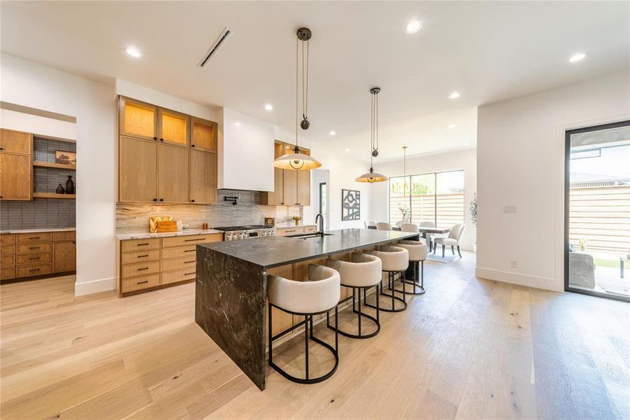 Kitchen with dark stone countertops, pendant lighting, light wood-style floors, and a large island