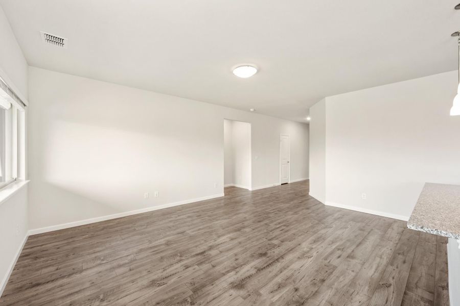 Empty living room with light wood-look floors, white walls, and open layout leading to hallway