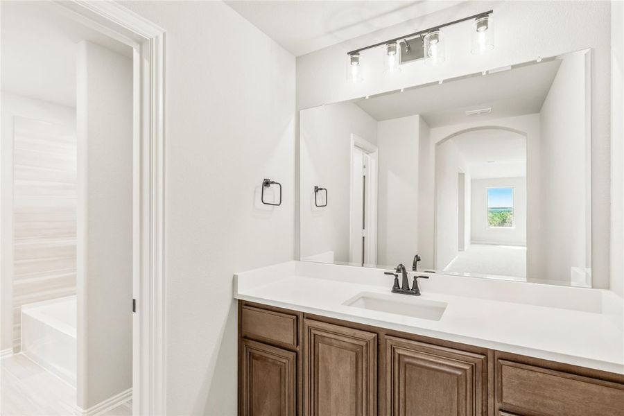 Bathroom vanity with dark wood cabinets, white countertop, single sink, and large mirror with overhead lighting Bathroom vanity with dark wood cabinets, white countertop, single sink, and large mirror with overhead lighting