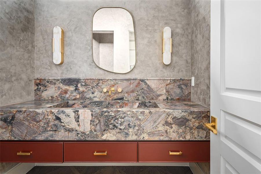 A striking blend of bold design and luxurious materials defines this secondary bathroom. The Marbella Quartzite apron-front marble vanity with an integrated sink serves as a dramatic focal point. Softly textured Venetian plastered walls and ceiling add depth and warmth, while Kelly Wearstler Melange Elongated sconces provide a sculptural lighting element. Below, white oak hardwood floors in a custom interlacing pattern complete the space with a refined and sophisticated touch.