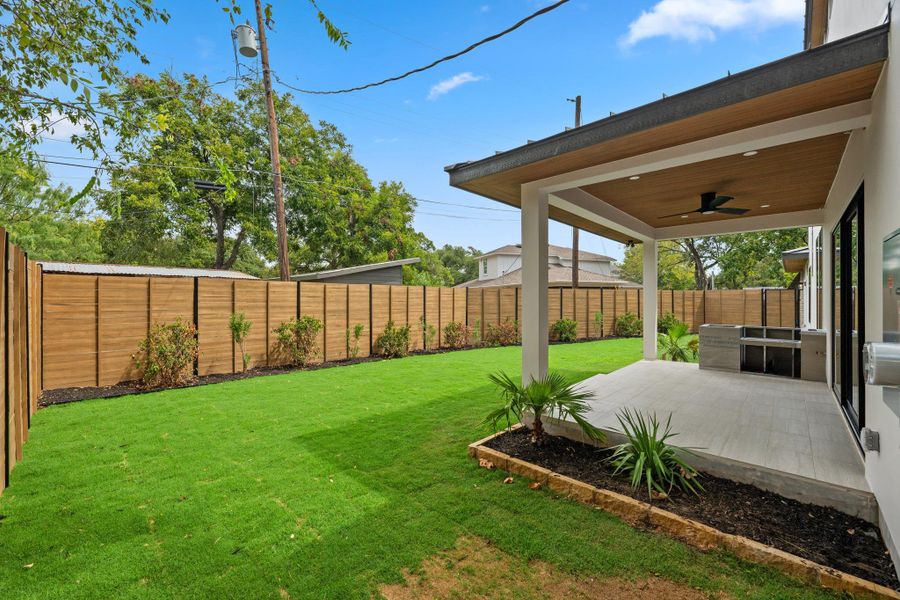 A spacious covered patio overlooks a grassy backyard enclosed by a tall privacy fence.