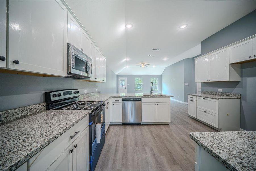 Kitchen with appliances with stainless steel finishes, white cabinets, light wood-style floors, light stone countertops, and recessed lighting Kitchen with appliances with stainless steel finishes, white cabinets, light wood-style floors, light stone countertops, and recessed lighting
