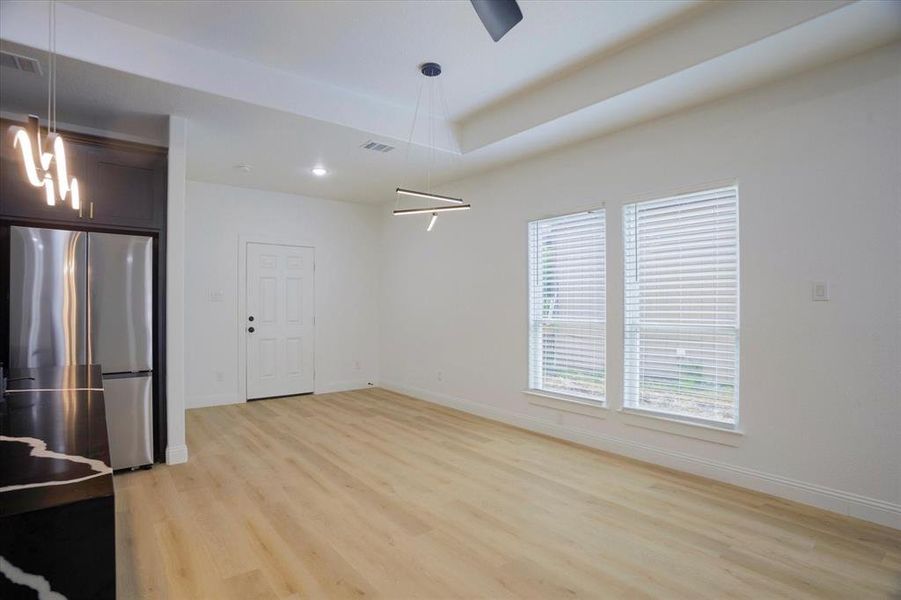 Unfurnished dining area with a notable chandelier, a raised ceiling, and light wood-type flooring