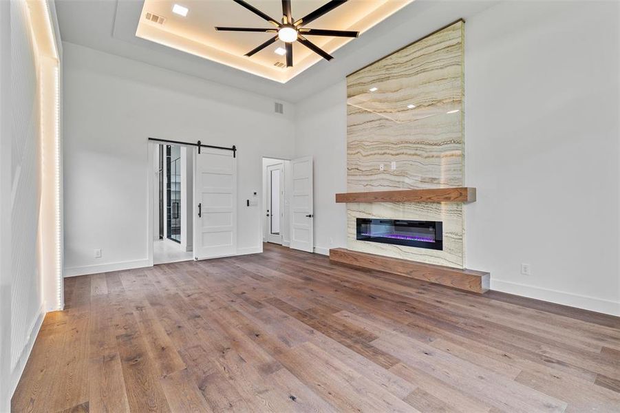 Unfurnished living room with a barn door, a raised ceiling, and hardwood / wood-style floors