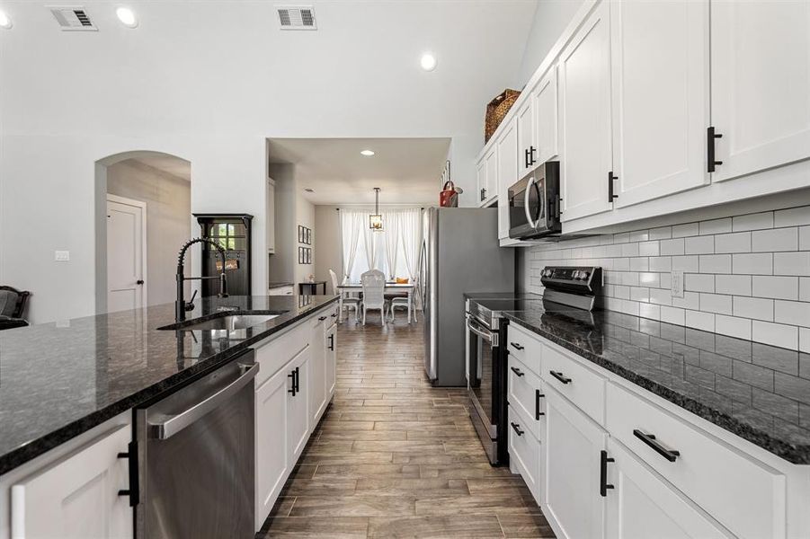 Kitchen featuring dark stone counters, white cabinets, appliances with stainless steel finishes, decorative light fixtures, and hardwood / wood-style floors