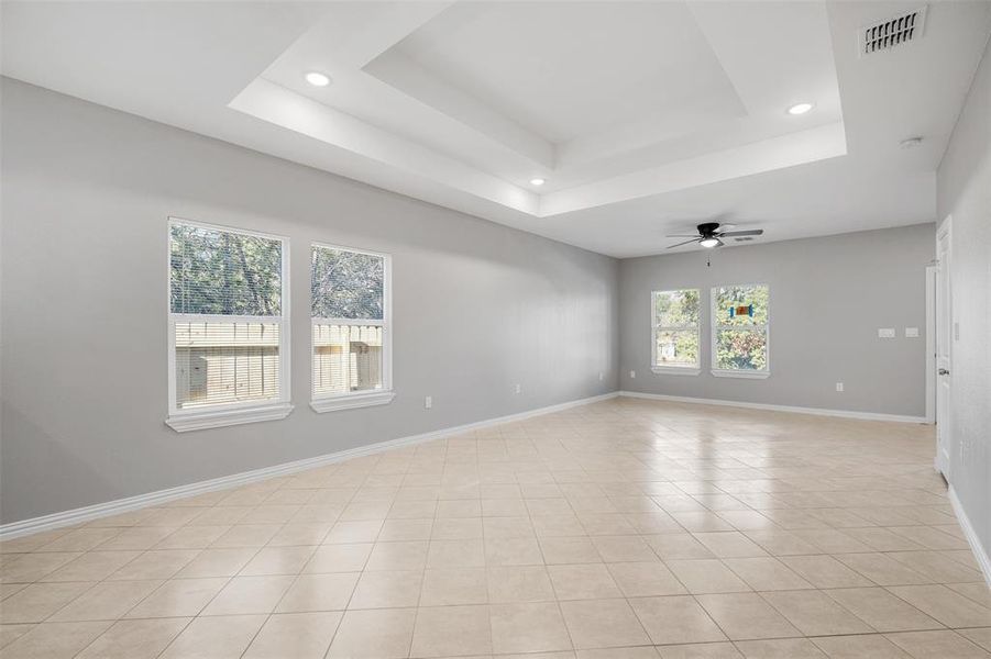 Tiled empty room featuring ceiling fan and a raised ceiling