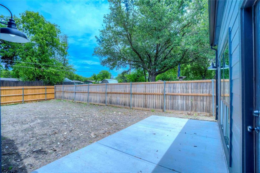 Spacious backyard featuring a new privacy fence, mature trees, and an exterior patio area