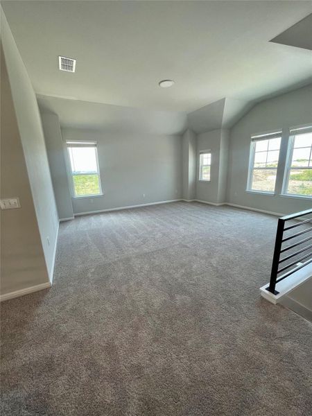 A spacious, carpeted room with large windows offering plenty of natural light. The neutral walls and ceiling add to the open feel, and a modern railing suggests a nearby staircase. Ideal for a living area or versatile space.