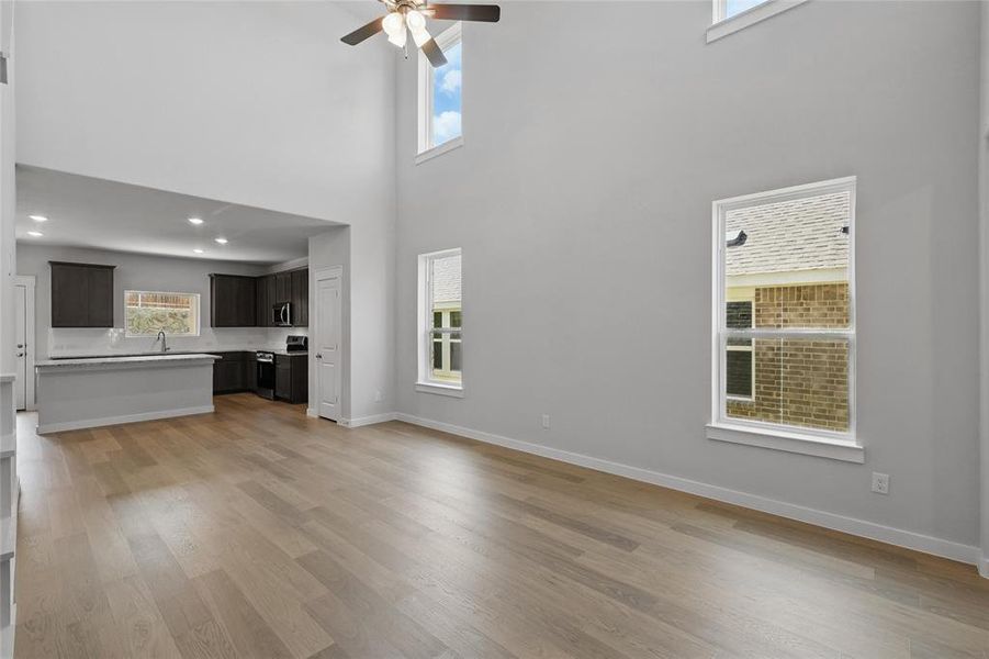 Unfurnished living room with ceiling fan, plenty of natural light, a high ceiling, and light wood-style floors
