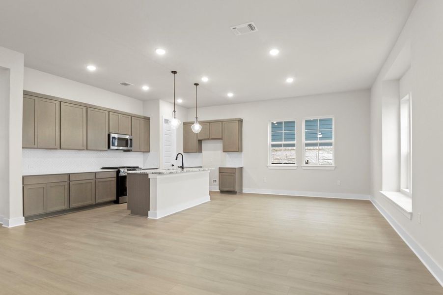 Kitchen featuring open floor plan, hanging light fixtures, stainless steel appliances, a kitchen island with sink, and light wood-style floors