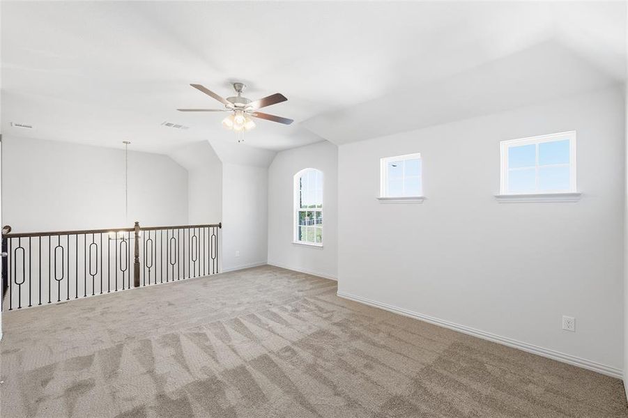 Carpeted empty room featuring vaulted ceiling and a ceiling fan