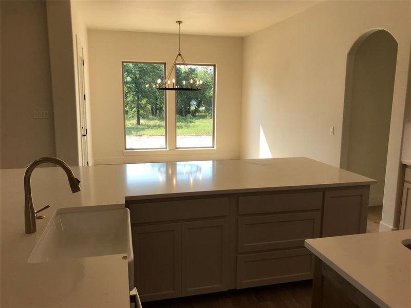 Kitchen with gray cabinetry, hanging light fixtures, arched walkways, dark wood-style flooring, and a chandelier