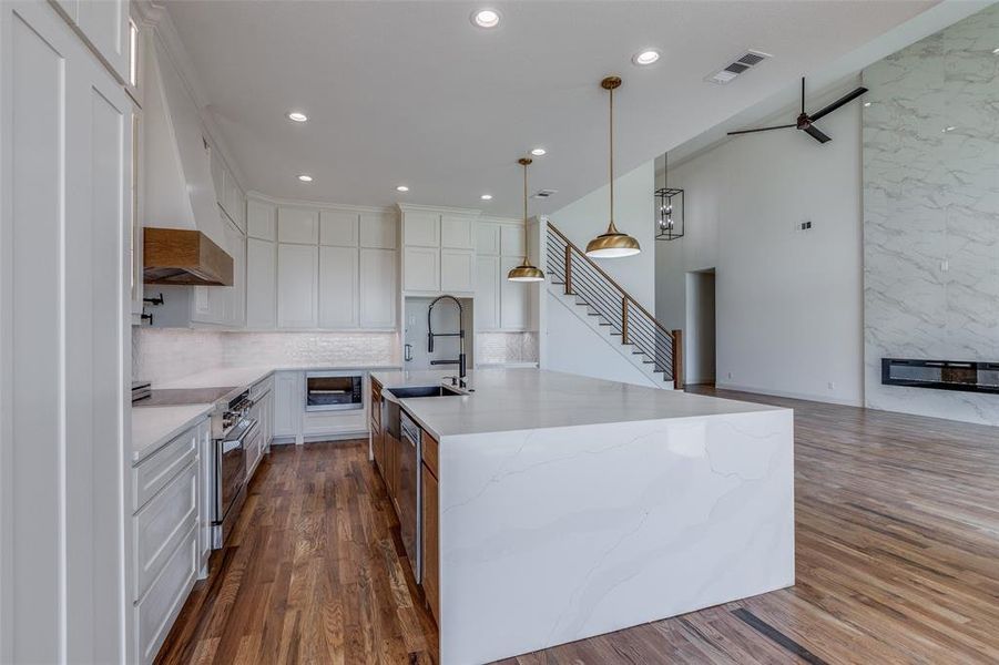 Kitchen featuring white cabinetry, an island with sink, ceiling fan, hardwood / wood-style flooring, and stainless steel range