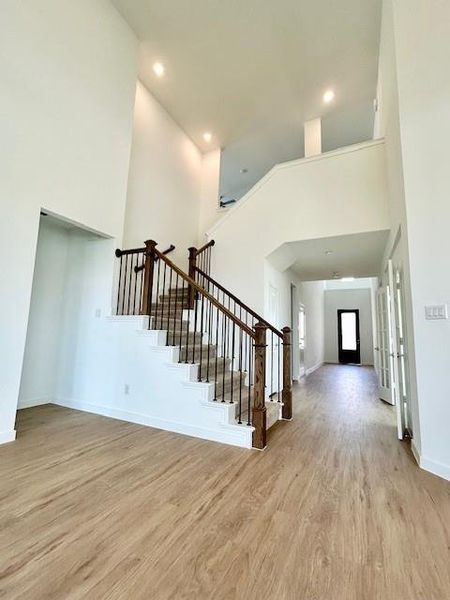 Two-story entryway featuring wood-finish flooring, a contemporary staircase with dark wood newel posts and iron balusters, recessed lighting, and white walls