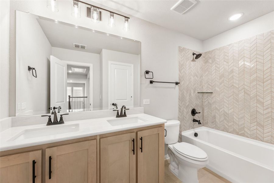 Bathroom with double sink vanity, wood cabinets, and tub-shower with herringbone tile surround