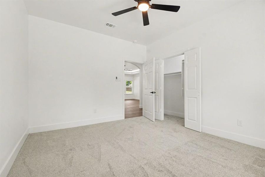This room features plush grey carpeting, white walls, and a ceiling fan with integrated lighting