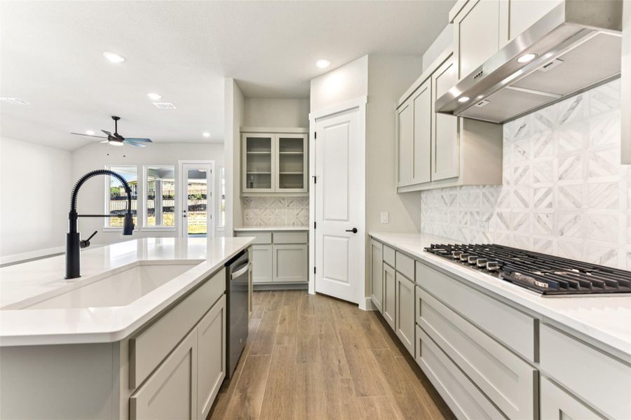 Kitchen with backsplash, wall chimney range hood, recessed lighting, gray cabinetry, and stainless steel appliances Kitchen with backsplash, wall chimney range hood, recessed lighting, gray cabinetry, and stainless steel appliances