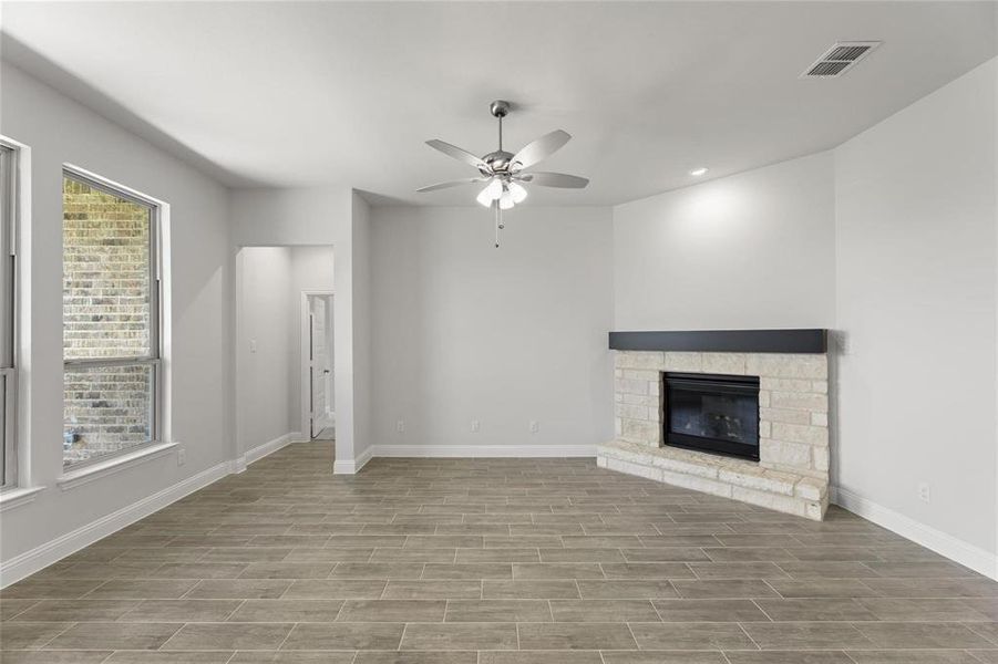 Unfurnished living room with baseboards, visible vents, a ceiling fan, a fireplace, and wood finished floors