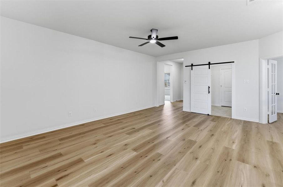 Spacious room featuring wood-finish flooring, a contemporary ceiling fan, and a barn door entry