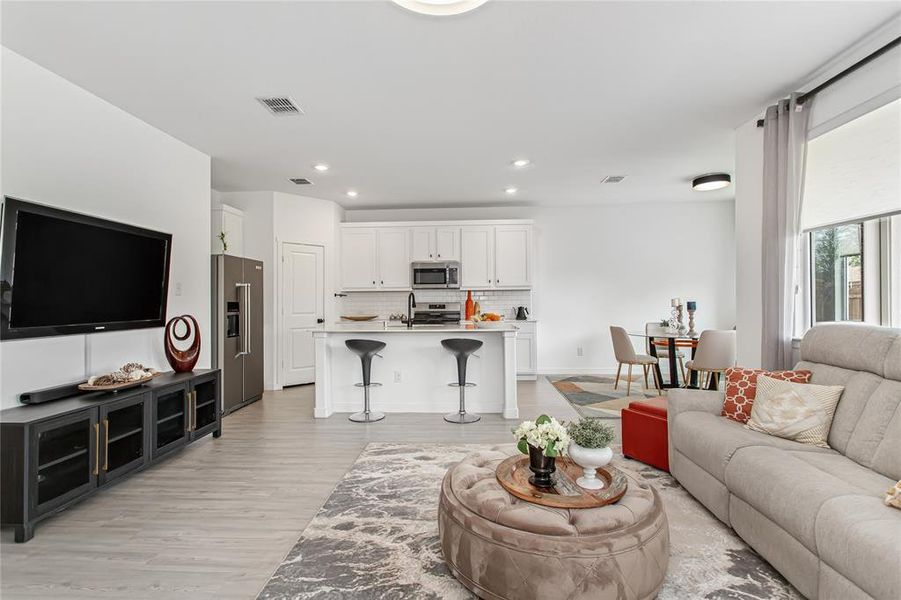 Open concept living area featuring light-colored flooring, a kitchen with white cabinetry and stainless steel appliances, and a dining area with a round table