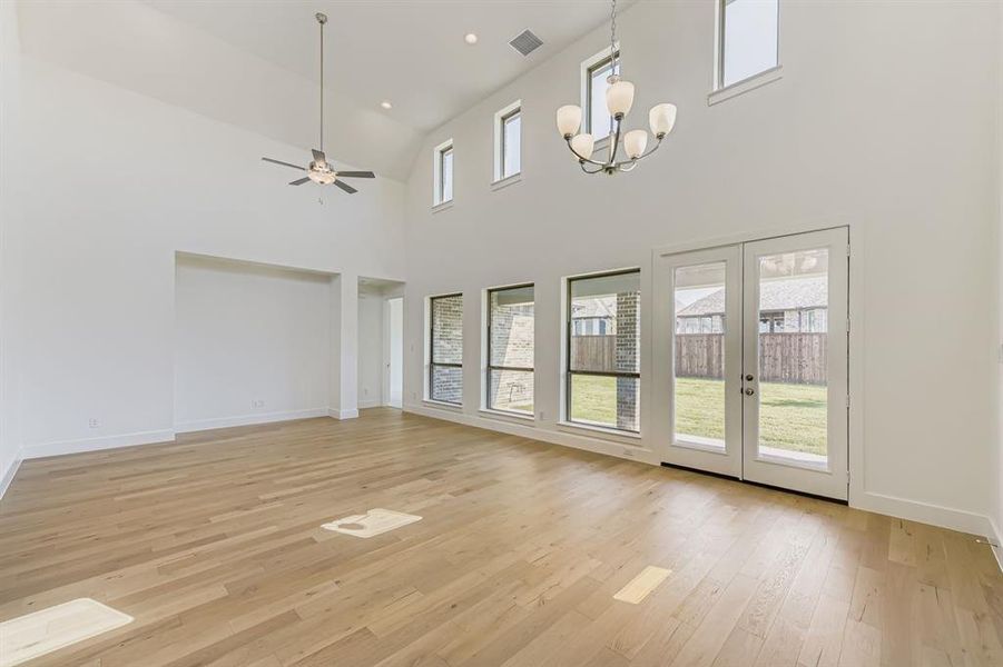 Unfurnished living room with light wood finished floors, a towering ceiling, a ceiling fan, recessed lighting, and french doors Unfurnished living room with light wood finished floors, a towering ceiling, a ceiling fan, recessed lighting, and french doors