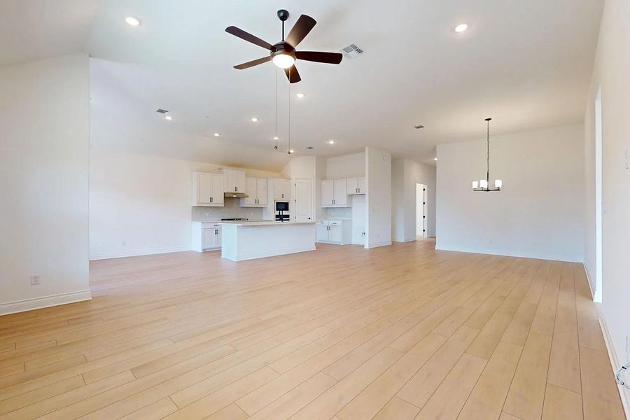 Expansive open-concept living area featuring light-toned wood flooring, a kitchen with white cabinetry and an island, a modern ceiling fan, and recessed lighting