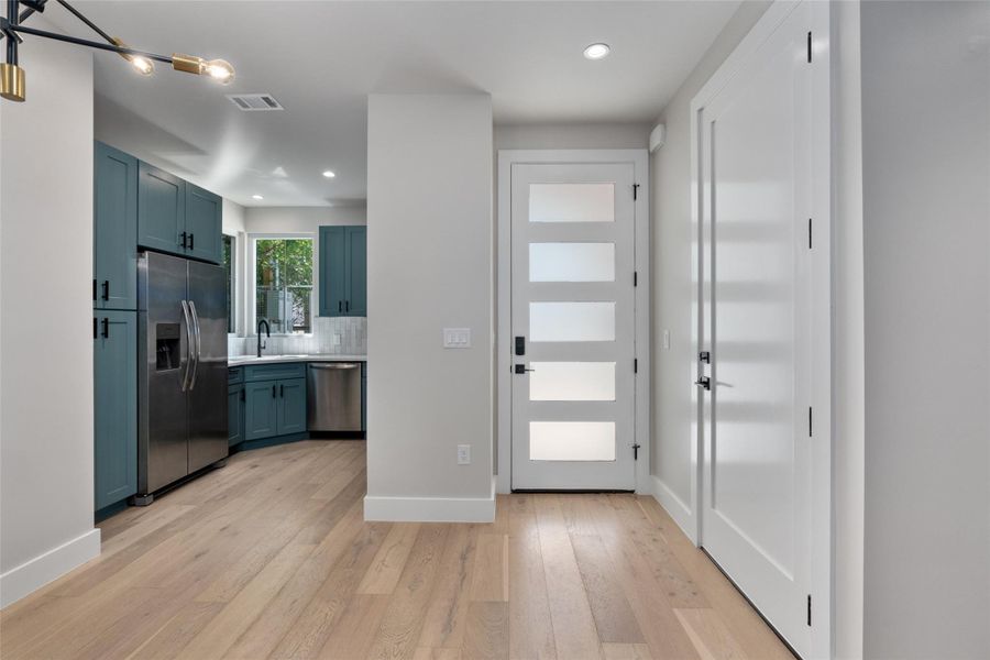 Light hardwood flooring extending into the kitchen, featuring teal Shaker style cabinetry, stainless steel appliances, and a subway tile backsplash Light hardwood flooring extending into the kitchen, featuring teal Shaker style cabinetry, stainless steel appliances, and a subway tile backsplash