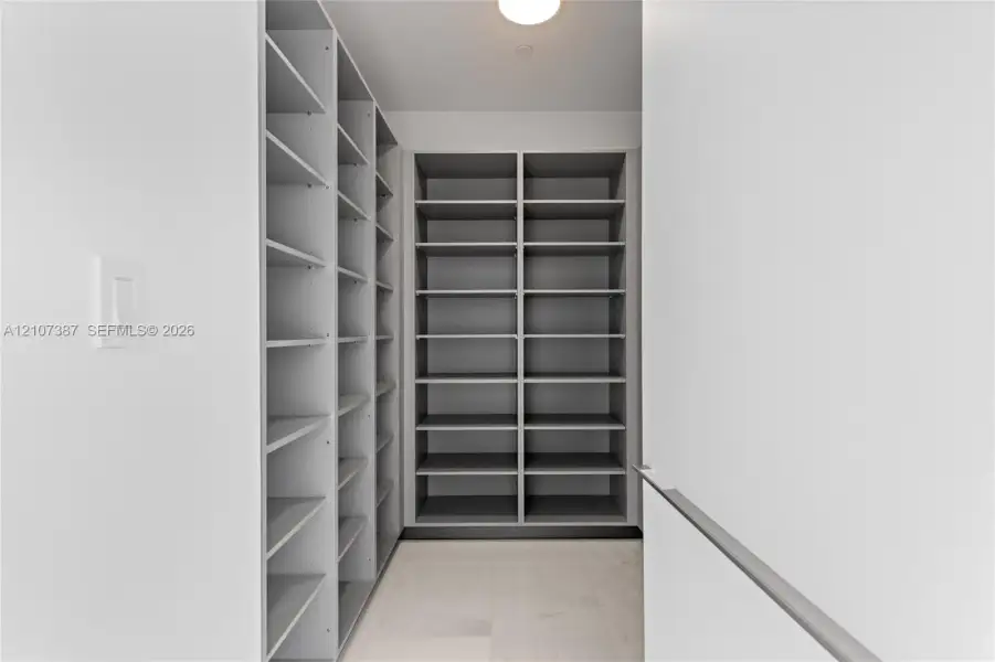 Custom walk-in storage featuring grey floor-to-ceiling shelving, light-toned tile flooring, and integrated overhead lighting
