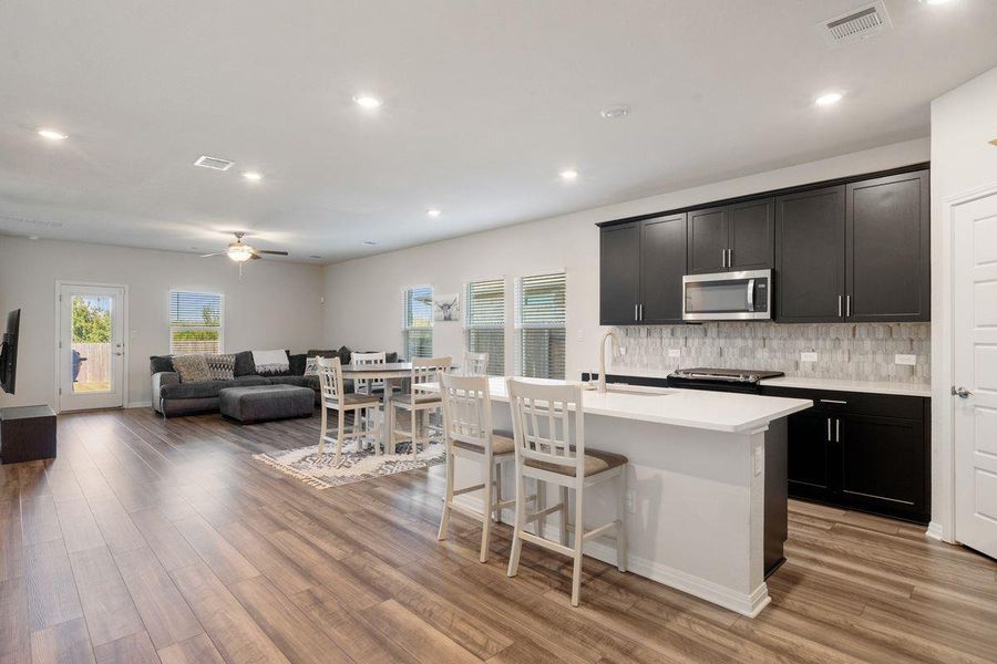 Bright open-concept floor plan featuring wood-look flooring, recessed lighting, and seamless flow from the kitchen to the living and dining areas. Bright open-concept floor plan featuring wood-look flooring, recessed lighting, and seamless flow from the kitchen to the living and dining areas.