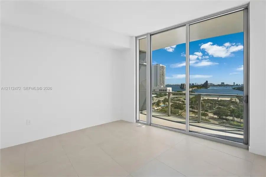 Floor-to-ceiling glass sliding doors, large-format tile flooring, and an expansive exterior balcony with water and city skyline outlooks