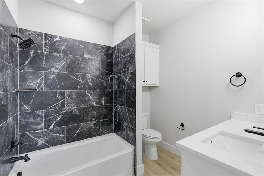 Bathroom featuring a white bathtub, dark marbled tile shower surround, matte black shower fixtures, a white vanity with an integrated sink and white countertop, and wood-finish flooring