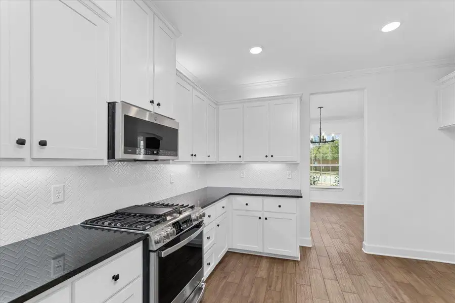 Kitchen featuring appliances with stainless steel finishes, dark countertops, a chandelier, light wood-style floors, and crown molding Kitchen featuring appliances with stainless steel finishes, dark countertops, a chandelier, light wood-style floors, and crown molding