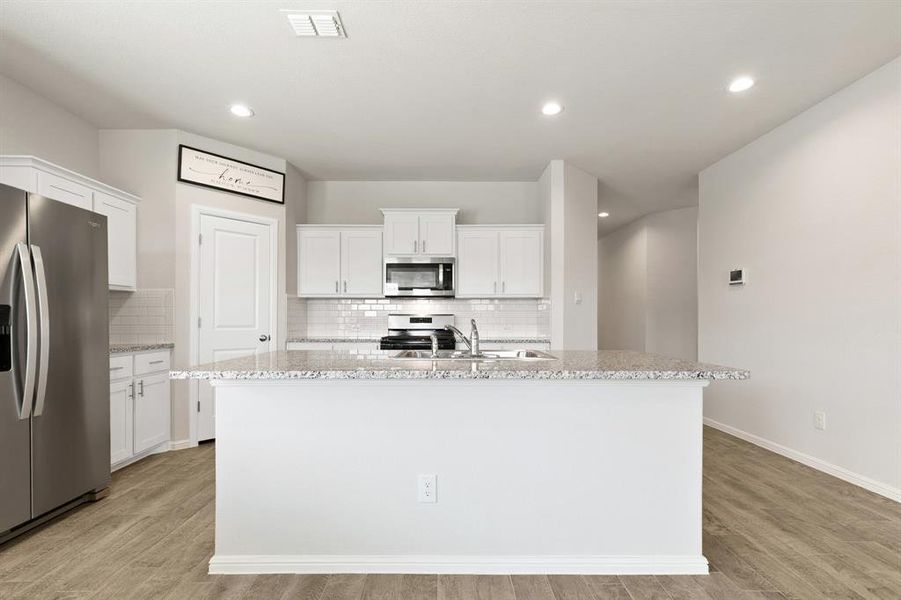 Kitchen featuring white cabinetry, stainless steel appliances, a center island with sink, light wood finished floors, and light stone countertops