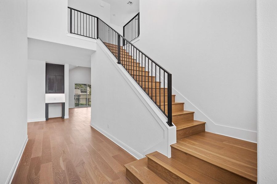 Stairway featuring wood finished floors, baseboards, and a high ceiling Stairway featuring wood finished floors, baseboards, and a high ceiling