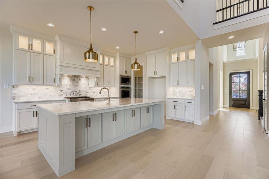 Kitchen featuring glass insert cabinets, white cabinetry, pendant lighting, a large island with sink, and recessed lighting