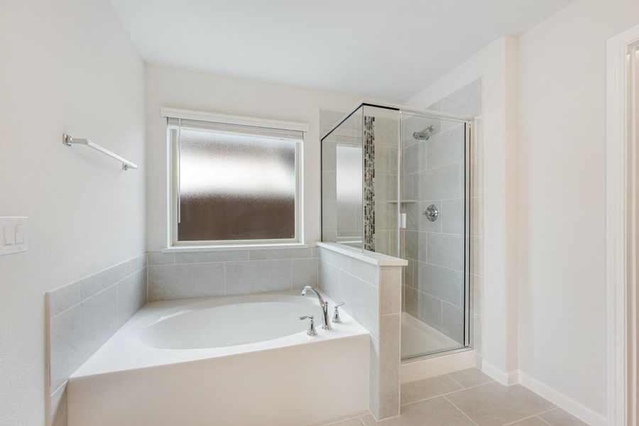 Bathroom with soaking tub, glass-enclosed shower, gray tile walls, and frosted window