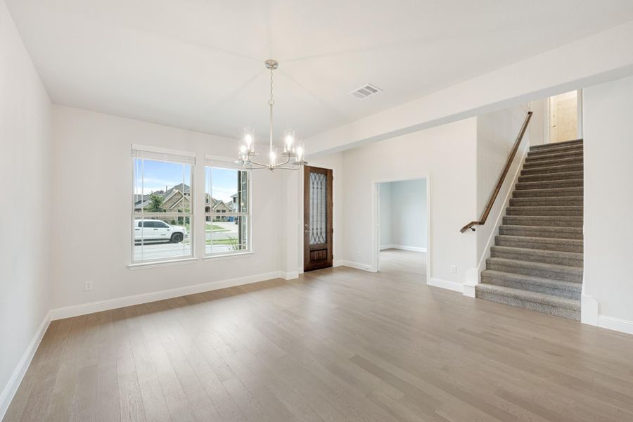Open living area with light wood floors, chandelier, front door, and carpeted staircase nearby Open living area with light wood floors, chandelier, front door, and carpeted staircase nearby