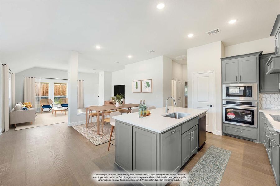 Open-concept kitchen with gray cabinets, center island with sink, and view into dining and living areas with hardwood floors