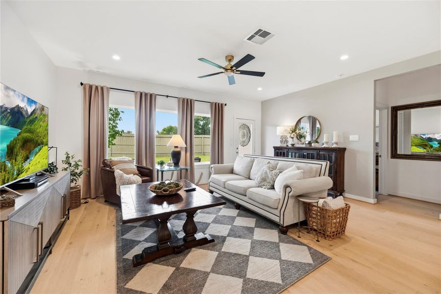 Living room with a designer accent wall, oversized windows and ceiling fan, open to the kitchen and dining area.