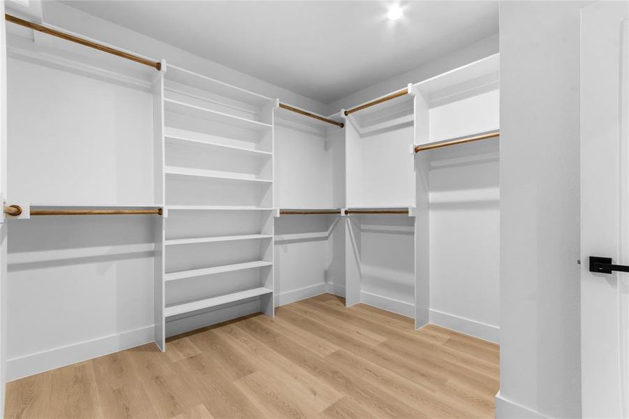 Walk-in closet featuring built-in white shelving, multiple hanging rods, recessed ceiling lighting, and wood-finish flooring Walk-in closet featuring built-in white shelving, multiple hanging rods, recessed ceiling lighting, and wood-finish flooring