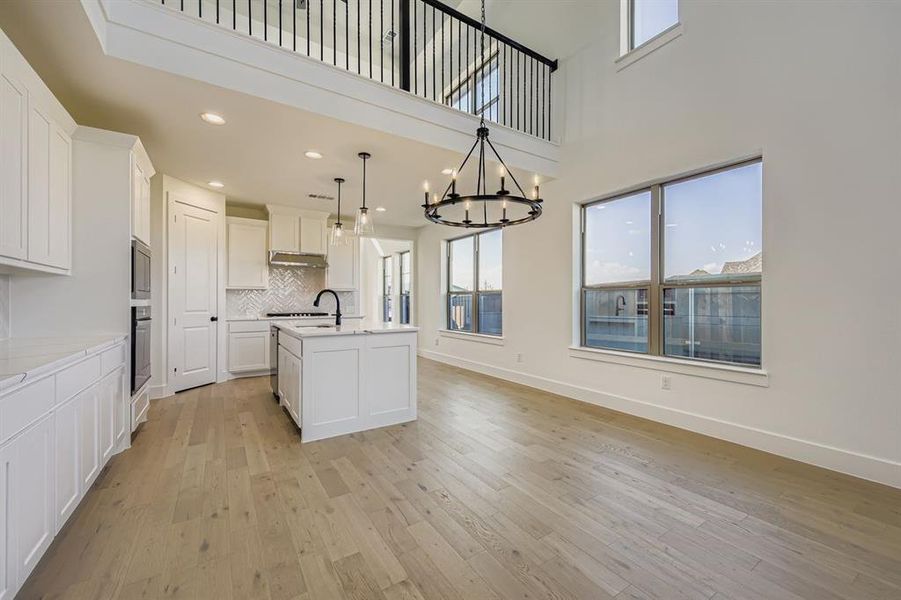 Kitchen with decorative backsplash, white cabinets, a chandelier, light wood finished floors, and a center island with sink