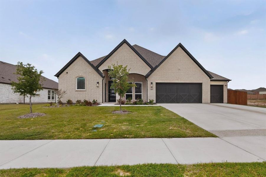 Contemporary brick exterior featuring a multi-gabled roofline, a three-car garage with decorative doors, and a concrete driveway Contemporary brick exterior featuring a multi-gabled roofline, a three-car garage with decorative doors, and a concrete driveway