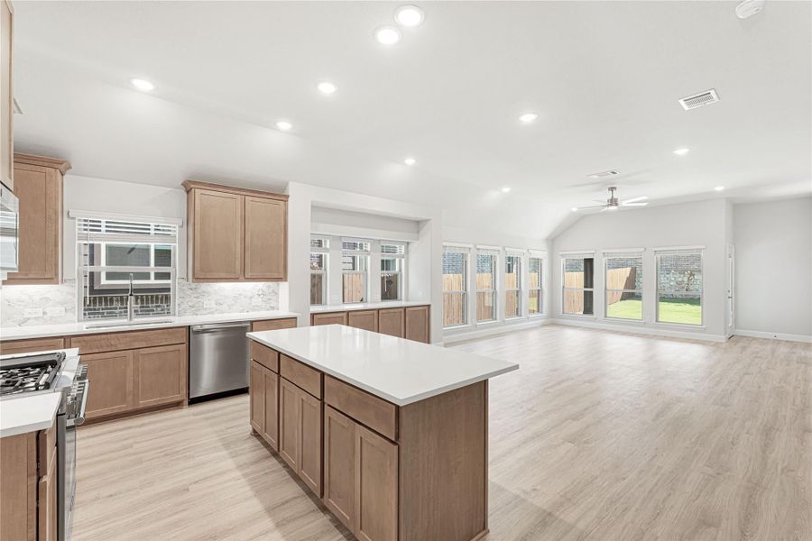 Open kitchen with wood cabinets, center island, and light hardwood floors flowing into living area Open kitchen with wood cabinets, center island, and light hardwood floors flowing into living area