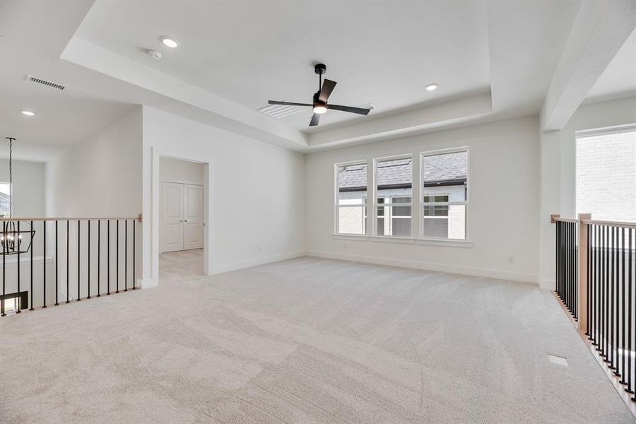 Unfurnished room with a raised ceiling, healthy amount of natural light, light colored carpet, a chandelier, and recessed lighting