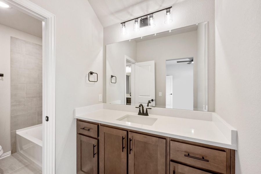 Bathroom with dark wood vanity, white countertop, large mirror, and tiled tub-shower combo visible through doorway.